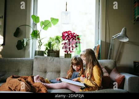 Sœurs lisant le livre sur le canapé Banque D'Images