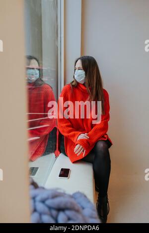 Woman wearing protective mask looking through window Banque D'Images