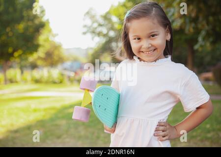 Bonne mignonne petite fille asiatique souriant à l'appareil photo en toute confiance, tenant son panneau de penny bleu menthe, copier l'espace. Petite fille joyeuse appréciant le skateboard Banque D'Images