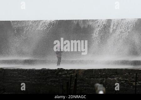 Lyme Regis, Dorset, Royaume-Uni. 18 décembre 2020. Météo Royaume-Uni. Un marcheur obtient un trempage d'une vague de tempête qui s'est lavé au-dessus du mur de Cobb Harbour à Lyme Regis dans Dorset un matin de vent et de pluie violents. Crédit photo : Graham Hunt/Alamy Live News Banque D'Images