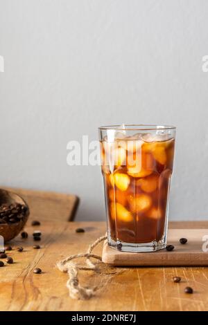 Café froid rafraîchissant dans un verre sur une planche en bois gros plan, fèves de cacao dans la noix de coco Banque D'Images