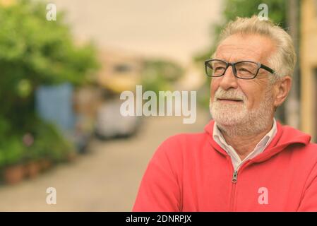 Close up of happy senior man smiling beau barbu en pensant et à la recherche jusqu'à l'extérieur avec des lunettes Banque D'Images