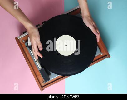 Les mains des femmes utilisent un lecteur de vinyle rétro sur fond bleu rose pastel. DJ. Vue de dessus Banque D'Images