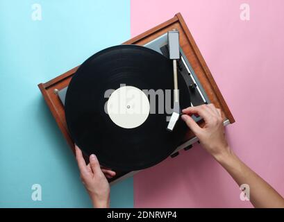 Les mains des femmes utilisent un lecteur de vinyle rétro sur fond bleu rose pastel. DJ. Vue de dessus Banque D'Images