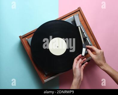 Les mains des femmes utilisent un lecteur de vinyle rétro sur fond bleu rose pastel. DJ. Vue de dessus Banque D'Images