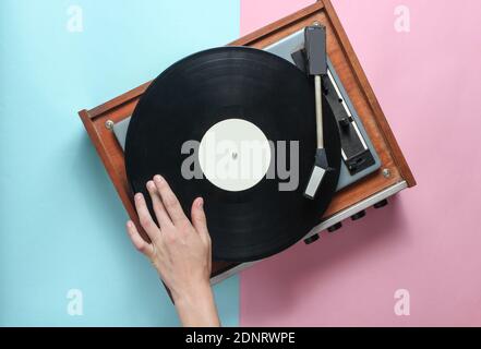 Les mains des femmes utilisent un lecteur de vinyle rétro sur fond bleu rose pastel. DJ. Vue de dessus Banque D'Images