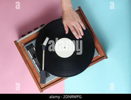 Les mains des femmes utilisent un lecteur de vinyle rétro sur fond bleu rose pastel. DJ. Vue de dessus Banque D'Images