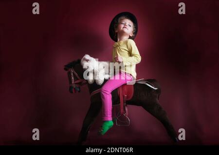 Portrait d'une fille sur un cheval à bascule avec elle ours en peluche Banque D'Images