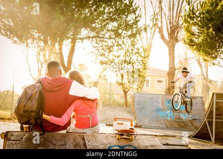 Vue arrière du jeune couple assis au parc Skateboard au coucher du soleil