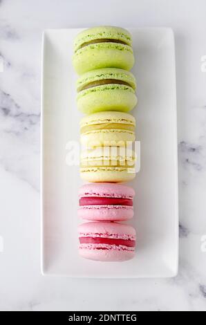 Vue aérienne de macarons aux fraises, pistaches et citron alignés sur une assiette Banque D'Images