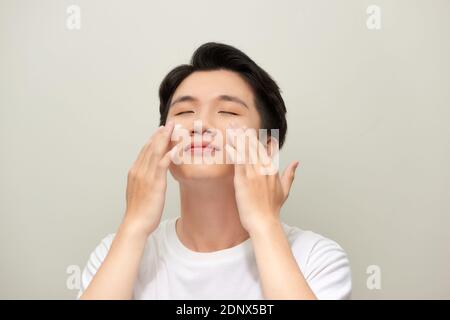 Portrait d'un jeune homme satisfait appliquant de la crème faciale isolé sur fond blanc Banque D'Images