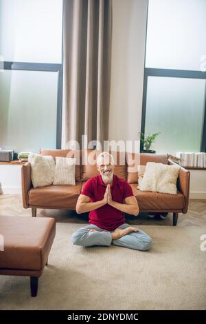 Homme aux cheveux gris assis sur le sol et faisant du yoga Banque D'Images