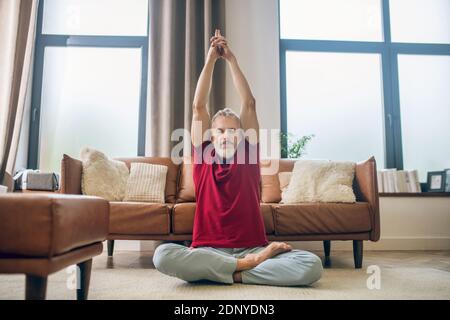 Homme aux cheveux gris assis sur le sol et faisant du yoga Banque D'Images