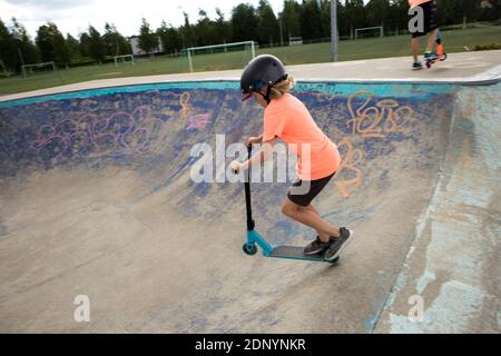 Garçon sur le scooter de poussée dans le parc de skateboard Banque D'Images