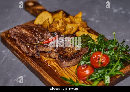 Steak de bœuf au piment fort sur une planche de bois avec des tranches de pommes de terre Banque D'Images