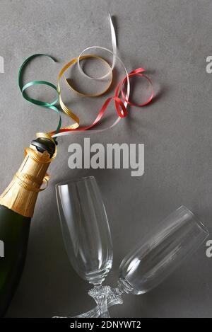 Bouteille de champagne avec rubans colorés et deux verres sur une table grise. Banque D'Images