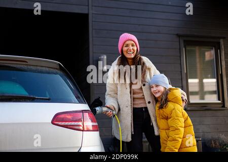 Femme avec fille charge la voiture électrique Banque D'Images