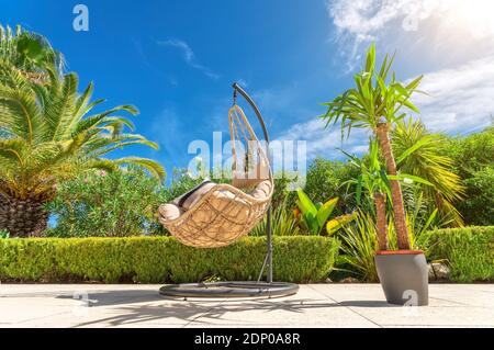 Chaise pivotante suspendue pour se détendre dans un jardin de luxe, vue sur le fond avec un pot de fleurs. Banque D'Images