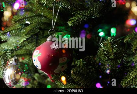 gros plan d'un arbre de noël rouge avec un bonhomme de neige suspendu d'un arbre de noël avec des lumières de bokeh étincelantes autour Banque D'Images