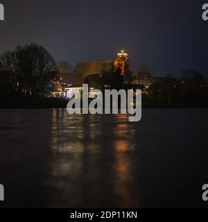 Les lumières de Noël d'une église se reflètent dans un lac dans l'obscurité Banque D'Images