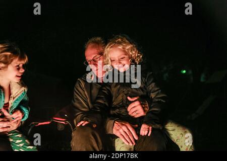 Petite-fille assise sur les genoux des grands-pères assis autour de la fosse de feu Banque D'Images