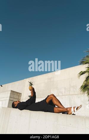 Jeune homme portant un caftan noir tenant un ananas Banque D'Images