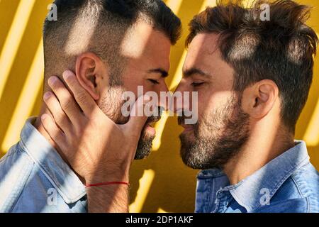 Couple gay debout face à face contre le mur jaune Banque D'Images