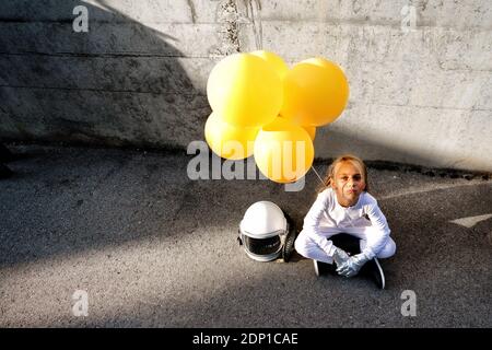 Vue en grand angle de la jeune fille tenant le ballon jaune assis contre mur pendant la journée ensoleillée Banque D'Images