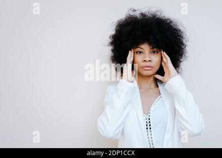 Portrait d'une femme afro-américaine aux cheveux afro-américains vêtus de costume blanc devant le mur urbain blanc à Grenade, Espagne Banque D'Images