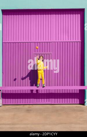 Bonne petite fille vêtue d'un équilibre jaune sur le bar à l'intérieur devant d'un garage violet qui jette de l'orange dans l'air Banque D'Images