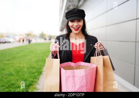 femme avec visage surpris et sacs de shopping dans la rue de la ville. Femme marchant à l'extérieur dans des vêtements noirs. Banque D'Images