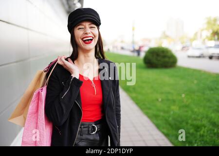 femme rit et tient des sacs de shopping dans la rue de la ville. fille marchant dehors dans des vêtements noirs. Banque D'Images