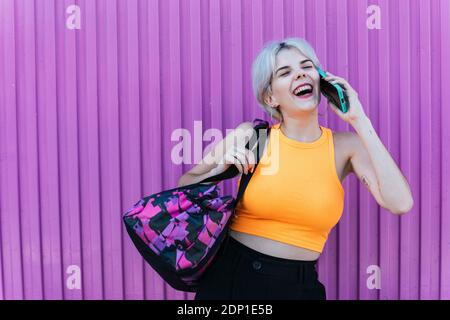 Portrait d'une femme à l'allure moderne et téléphone portable à l'arrière-plan urbain violet à Grenade, Espagne. Femme jeune blonde 'Gen Z' coloré purble mobile Banque D'Images