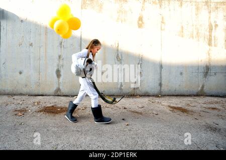 Petite fille marchant avec un casque d'espace et tenant le ballon dessus rue pendant la journée ensoleillée Banque D'Images