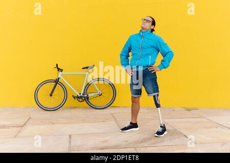 Homme avec un membre et un pied artificiels debout à la main hanche contre paroi jaune Banque D'Images