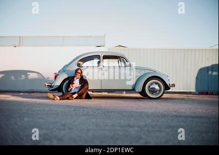 Senior man sitting in front of vintage car using mobile phone Banque D'Images