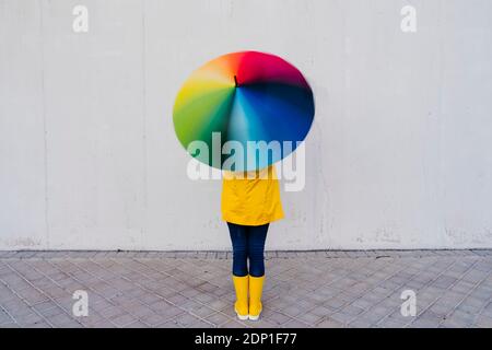 Femme tenant un parapluie coloré debout devant un mur gris sur le sentier Banque D'Images