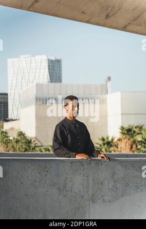 Jeune homme portant un caftan noir derrière un mur en béton Banque D'Images