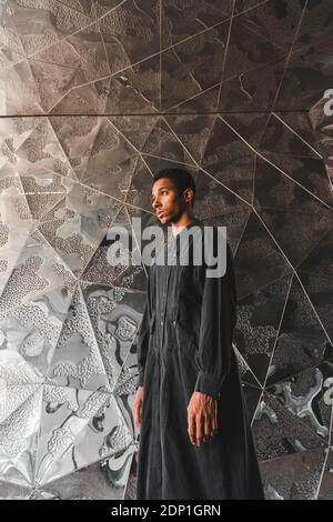 Jeune homme portant un caftan noir debout sur un mur structuré Banque D'Images