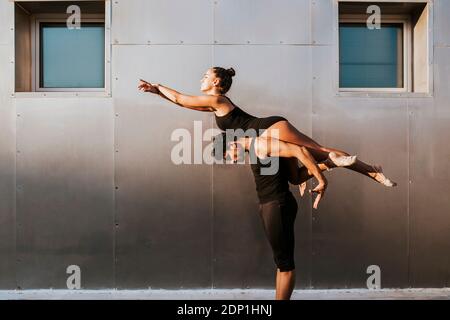 Gymnaste mâle portant la femme sur les épaules tout en pratiquant la posture de danse par mur Banque D'Images