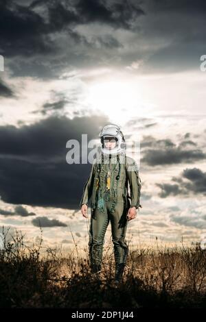 Homme posant habillé comme un astronaute sur une prairie avec des nuages dans l'arrière-plan Banque D'Images