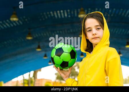 Portrait d'une petite fille portant une veste à capuchon jaune tenant le soccer bille Banque D'Images