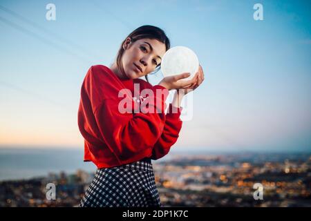 Femme tenant un équipement d'éclairage lumineux en forme de lune au crépuscule Banque D'Images