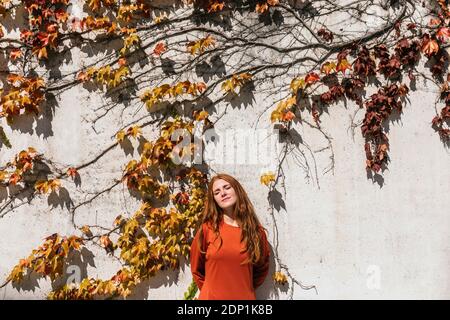 Femme avec les yeux fermés et les mains derrière le dos debout contre mur ivy Banque D'Images