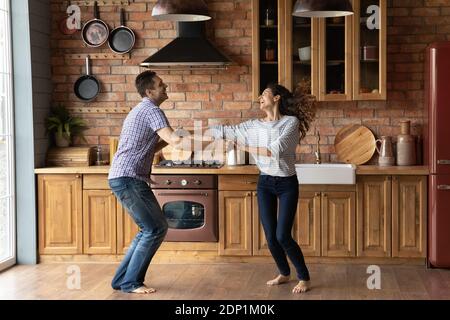 Un couple millénaire joyeux dansant dans la cuisine, enthousiaste à l'idée de se déplacer Banque D'Images