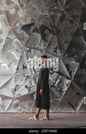 Jeune homme portant un caftan noir debout sur un mur structuré Banque D'Images