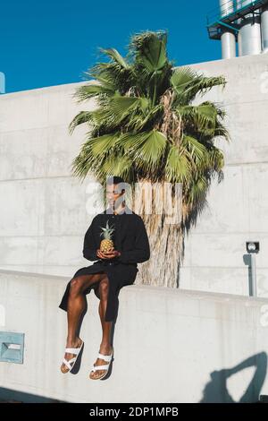 Jeune homme portant un caftan noir tenant un ananas Banque D'Images