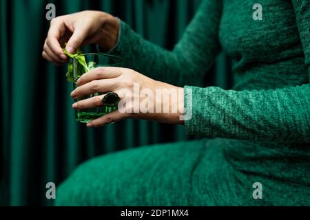 Section médiane de la femme tenant un verre de boisson de cocktail assis contre rideau Banque D'Images