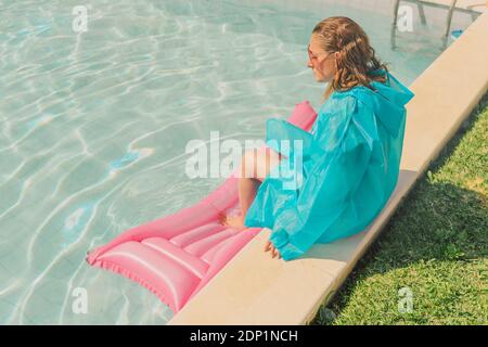 Femme sous un manteau de pluie bleu assis au bord de la piscine Banque D'Images