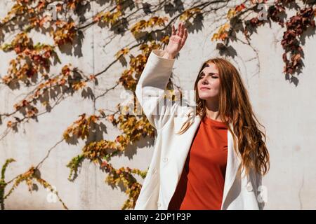 Jeune femme avec la main levée debout contre le mur de lierre Banque D'Images